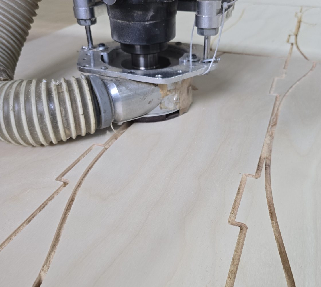A CNC router mid-cut, with slat profiles already cut into the plywood sheet.